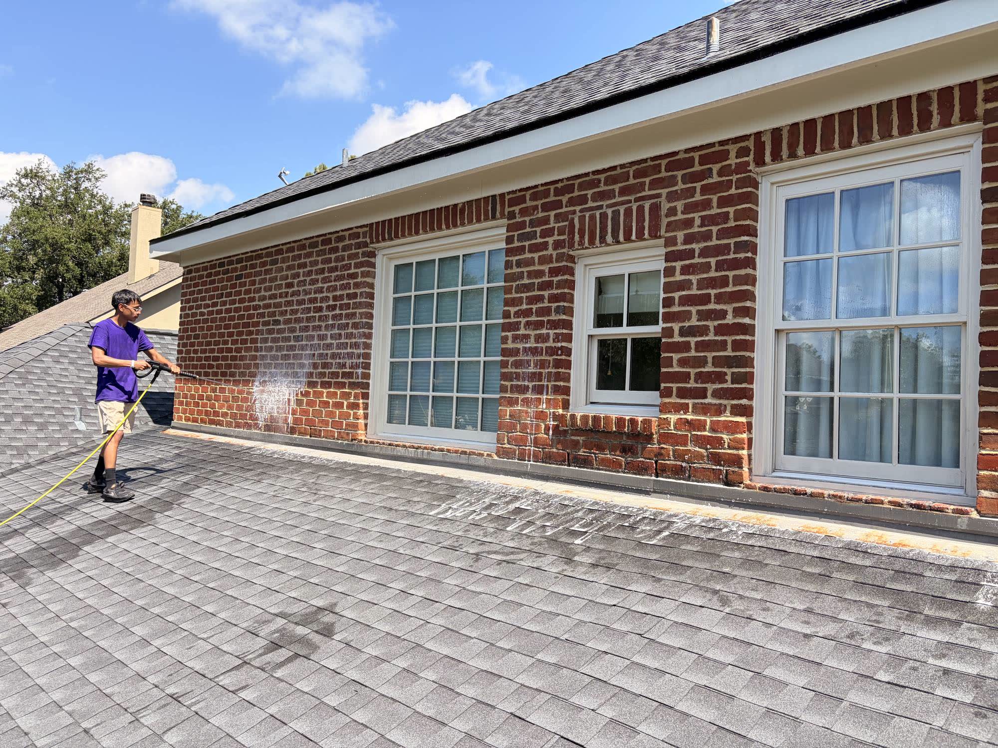 Wicked Window Wash technician soft washing a brick wall from the roofline in Houston