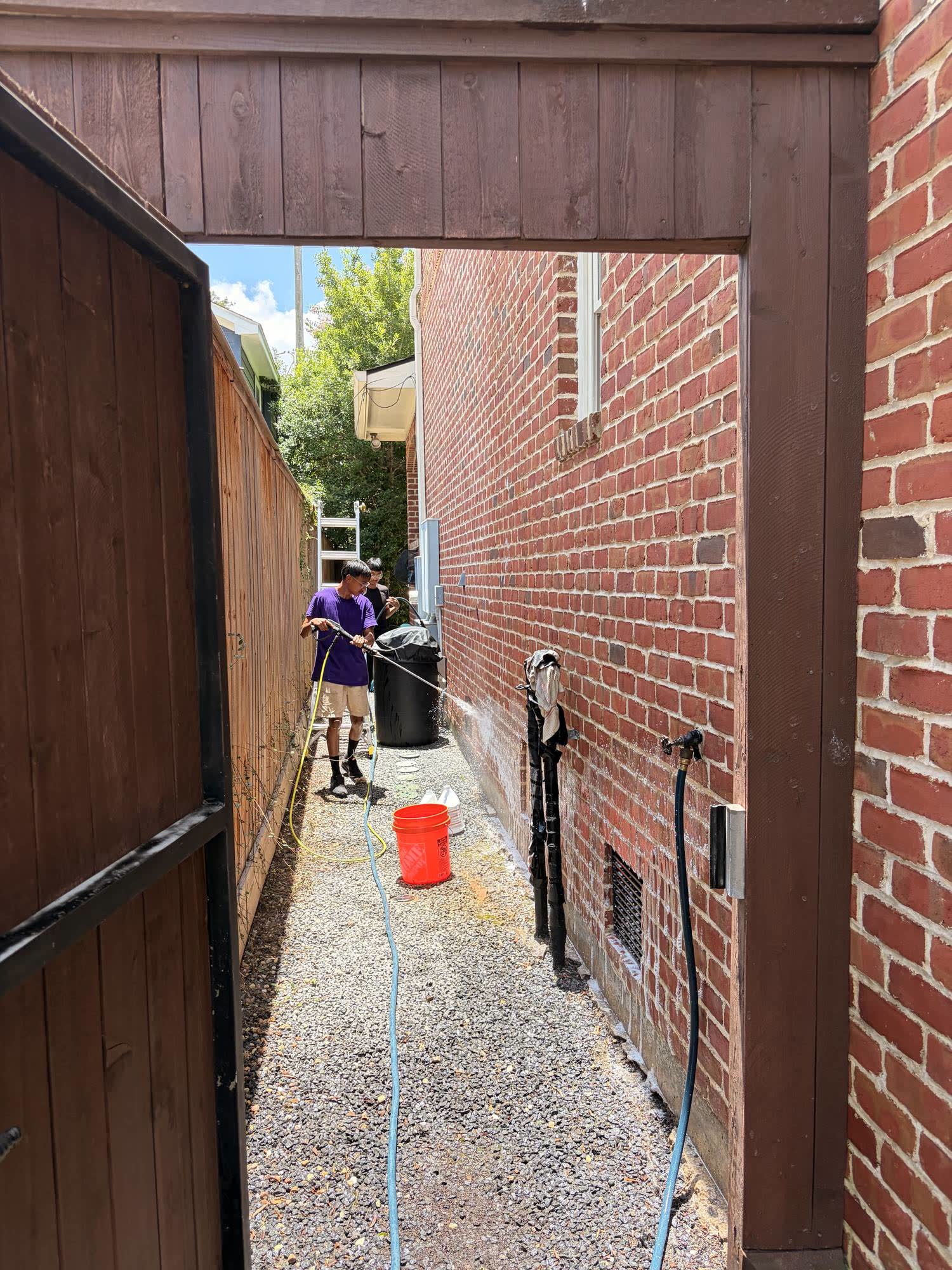 Low-pressure soft wash lifting algae from a shaded brick side wall