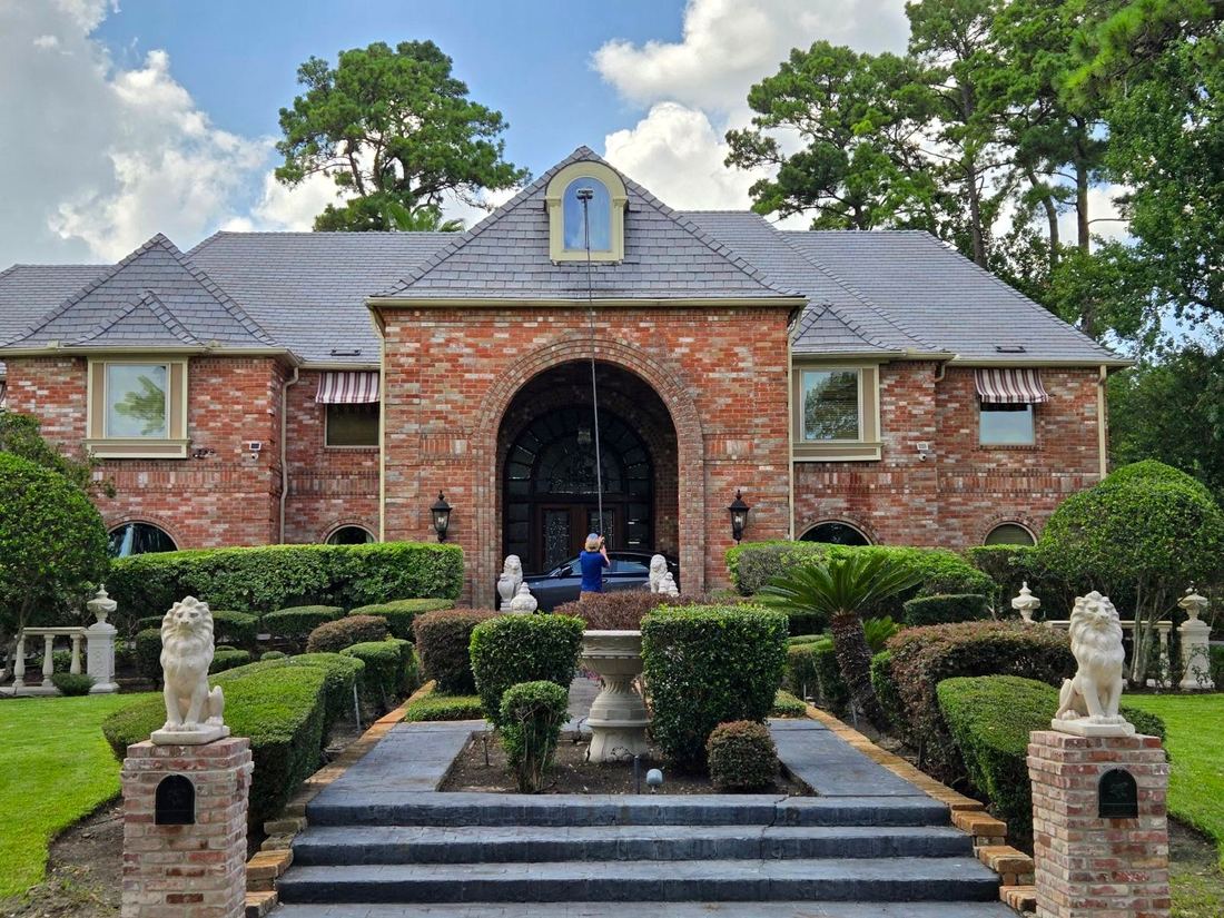 Water-fed pole cleaning the arched entry windows of a grand Houston brick estate